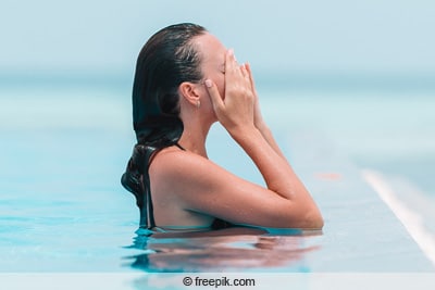 Chlorgehalt - Frau im Pool reibt sich Augen