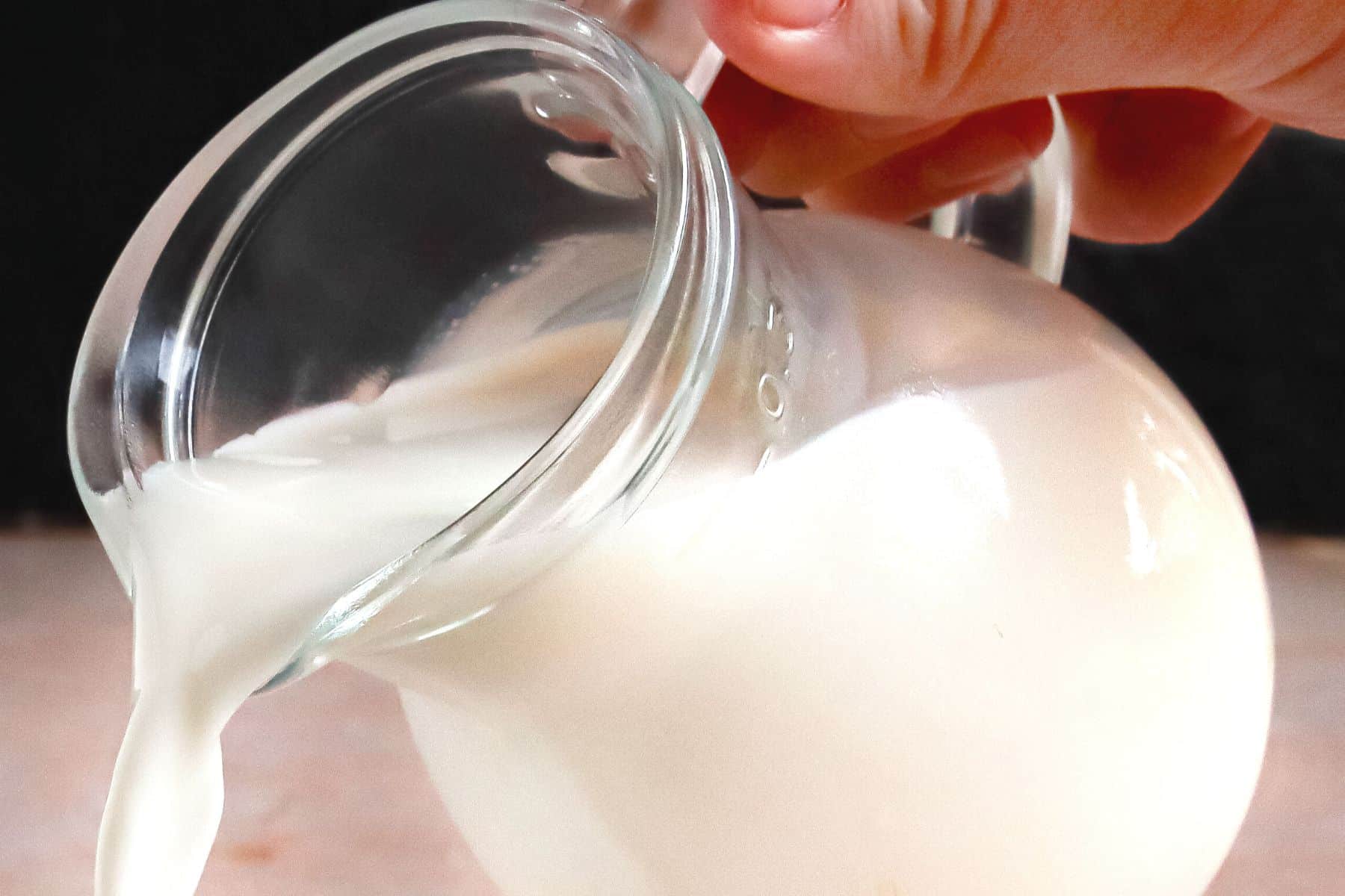 Hand gießt Milch aus Glaskanne