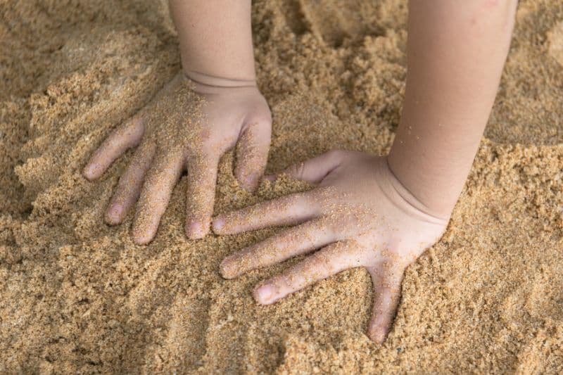 Kind spielt mit Händen im Sand